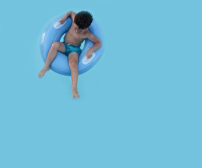 Boy sitting in flotation ring in pool.