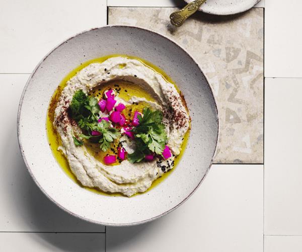 Over the top shot of a cream-coloured eggplant dip, drizzled generously with olive oil and garnished with bright-pink diced pickled turnips and coriander leaves.