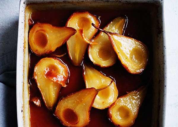 A white square dish holding halved roasted pears in a dark-brown maple syrup.