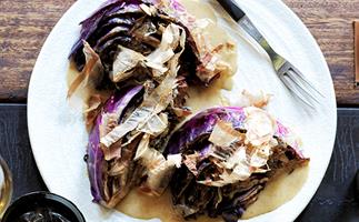 Wedges of purple cabbage, sprinkled with bonito flakes, on a white plate, with a fork