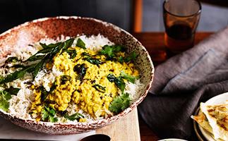 A speckled brown bowl holding white rice, yellow-coloured dhal, and curry leaves.