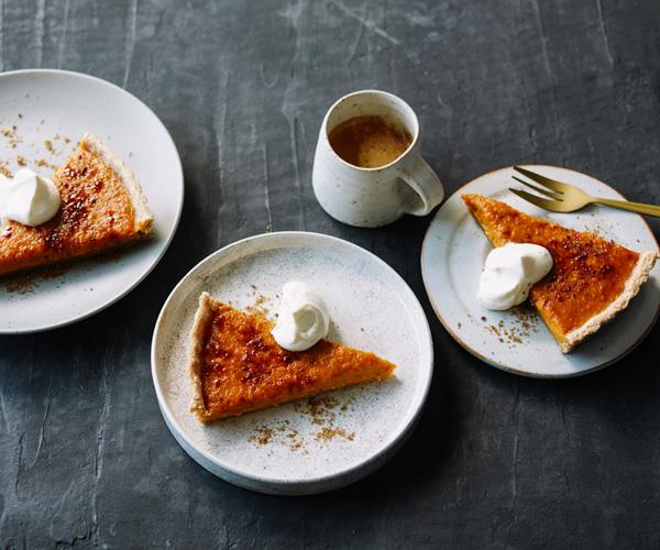 Three white round plates, each holding a triangular slice of golden-baked pumpkin pie, dusted with cinnamon, and served with a dollop of cream.