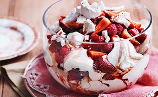 A large, deep, round and glass bowl holding a delightful mess of meringue, whipped cream, raspberries and sliced strawberries. Try resisting.