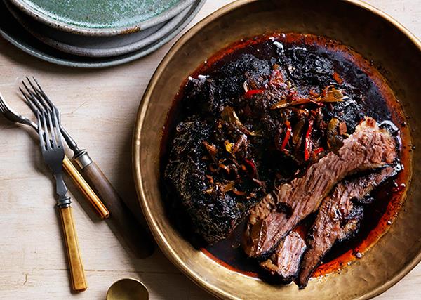 Over-the-top shot of a bronze bowl with braised, blackened beef brisket, garnished with red chillies.