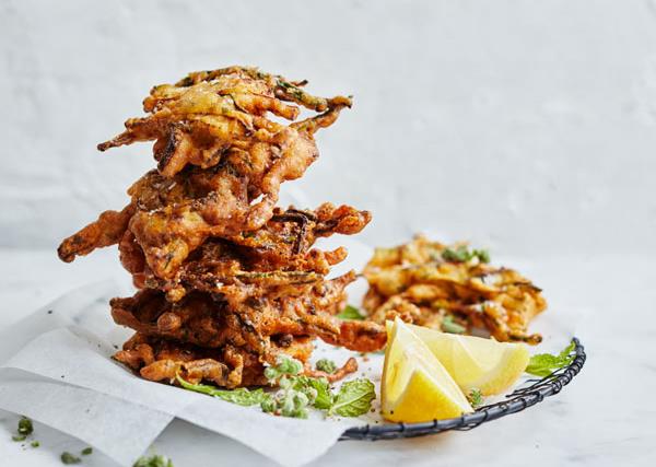 Fried zucchini fritters with wedges of lemon, stacked on a plate lined with white baking paper, on a white background.