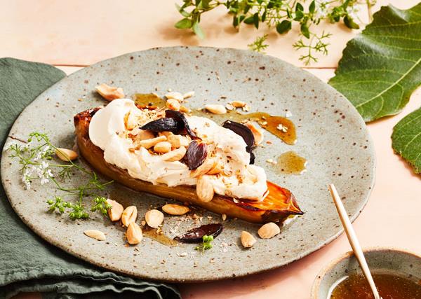 A thick slice of charred eggplant, topped with a thick white sauce and almonds, on a marbled grey plate, surrounded by a green linen napkin and green foliage.