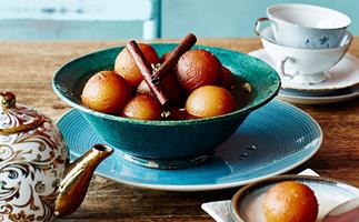 A aqua-blue bowl holding spheres of gulab jamun in syrup, garnished with two cinnamon sticks