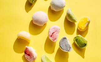 An assortment of pink, green, yellow and purple mochi-covered ice-cream on a bright yellow background