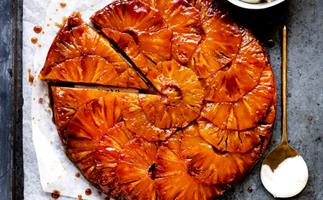 Upside-down tart with caramelised pineapple slices layered on top, with a triangular slice detached from the tart. 