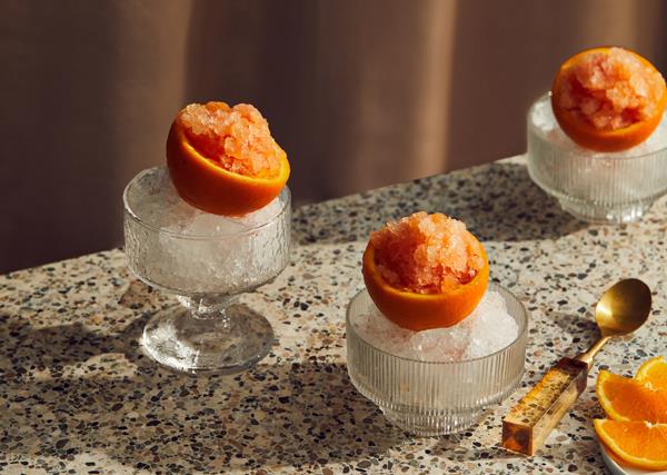 Three crystal glass cups filled with shaved ice, topped with hollowed-out orange halves filled with orange granita.