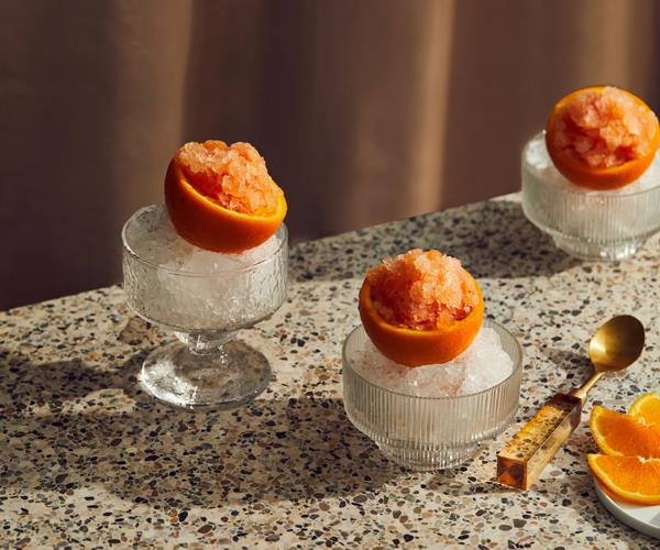 Three crystal glass cups filled with shaved ice, topped with hollowed-out orange halves filled with orange granita.