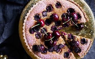 Over-the-top shot of a circle tart studded with whole and halved cherries, dusted with icing sugar.