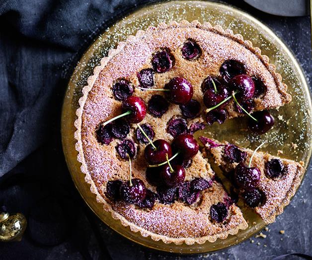 Over-the-top shot of a circle tart studded with whole and halved cherries, dusted with icing sugar.