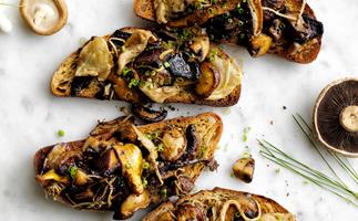 Four slices of toast topped with sautéed mixed mushrooms, on a white and grey marble surface.