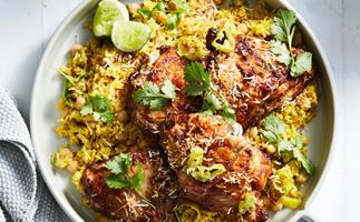 Close-up of a plate of roast chicken thighs on a bed of yellow pilaf, garnished with coriander leaves and lime wedges.