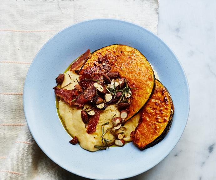 Wedges of roasted pumpkin, fried speck, chopped almonds and polenta on a eggshell blue round plate on a marble background.