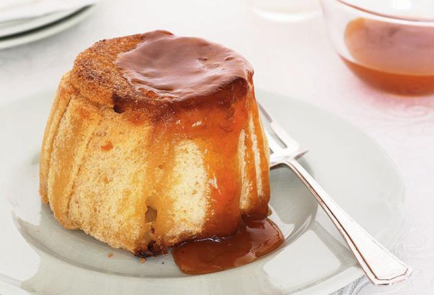 A steamed round apple pudding, drizzled with warm apricot jam, on a round plate with a silver fork on the right. 