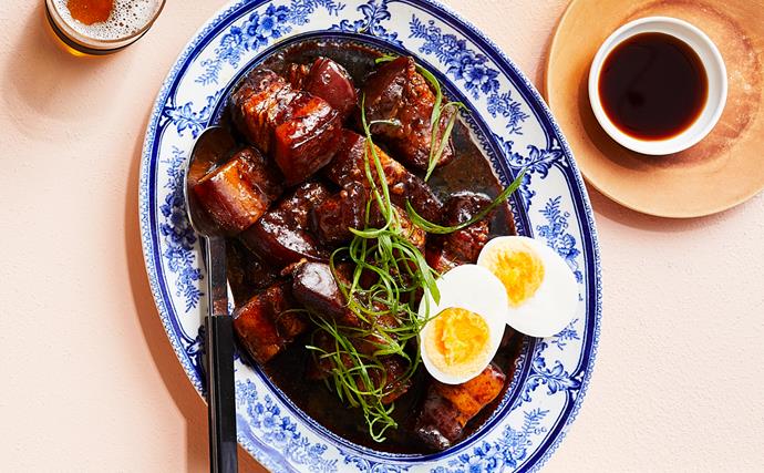 Overhead shot of a ornamental blur and white oval plate holding soy braised pork belly and a halved hard-boiled egg.