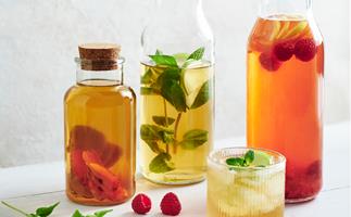 Three glass carafes plus a short ridged glass holding kombucha, garnished with mint and strawberries