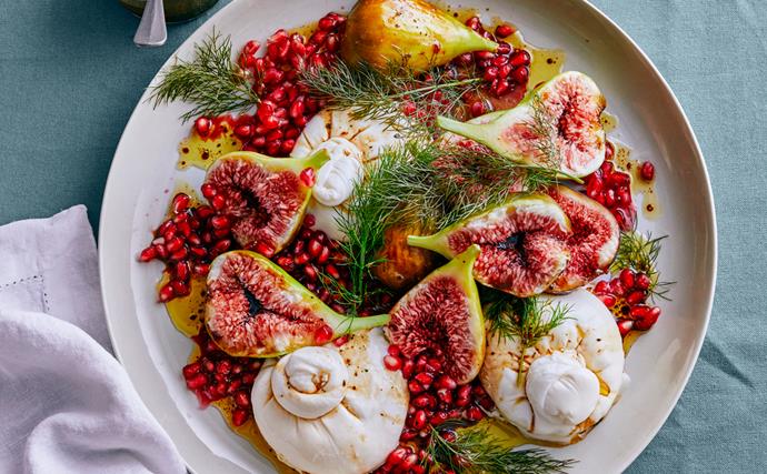 A large plate of figs with burrata, garnished with pomegranate arils and fennel sprigs 