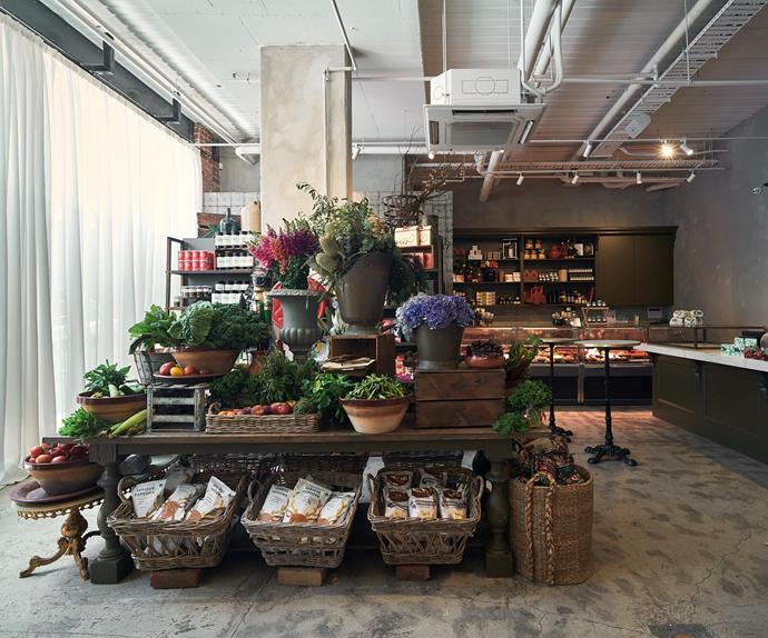 There's a table full of flowers and vegetables, below it is a range of vegan products. In the background, there is a shop counter with shelves behind it. 