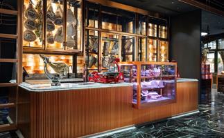 A wooden counter with marble countertops. Behind there are glass cabinets filled with dried and cured meats. 