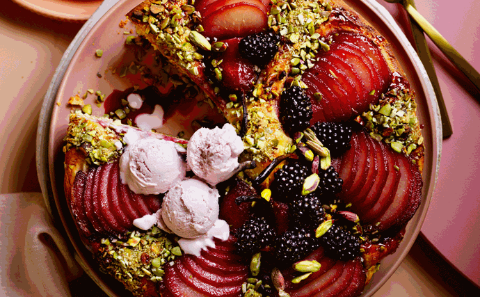 Cake with a slice cut out of it, topped with slices of pear, chopped pistachios, blackberries, and gin ice cream.