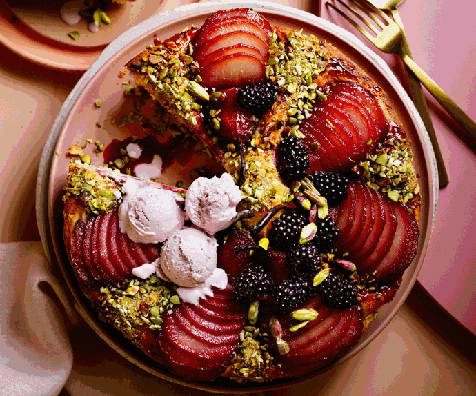Cake with a slice cut out of it, topped with slices of pear, chopped pistachios, blackberries, and gin ice cream.