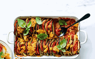 Thin slices of tomato, potato, eggplant, and zucchini layered horizontally in a shallow dish topped with toasted breadcrumbs.