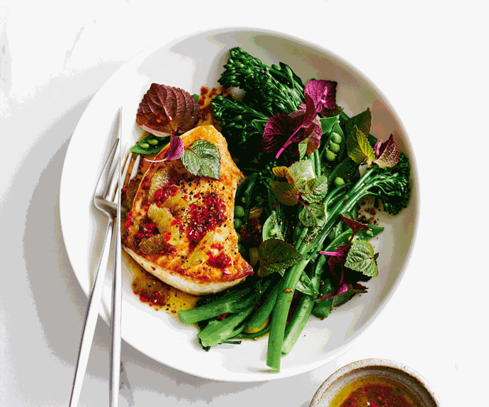 Piece of swordfish with chilli dressing served with steamed broccolini and microgreens salad on a white plate.