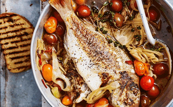 Whole baby snapper in a pan with tomato, fennel, and basil sauce. Large slices of charred sourdough on either side of the pot.