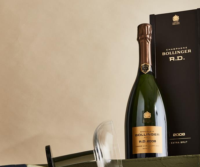 Bottle of the new Bollinger R.D. 08 Champagne release in between a sideways Champagne glass and the Bollinger R.D. packaging