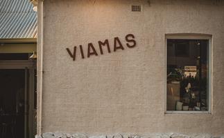 Exterior of stone-coloured building with sign reading 'YIAMAS' and a portrait window and metal roof