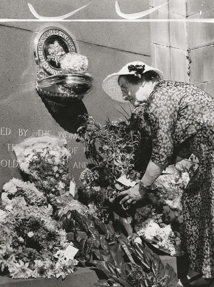 A woman lays a wreath against a memorial.