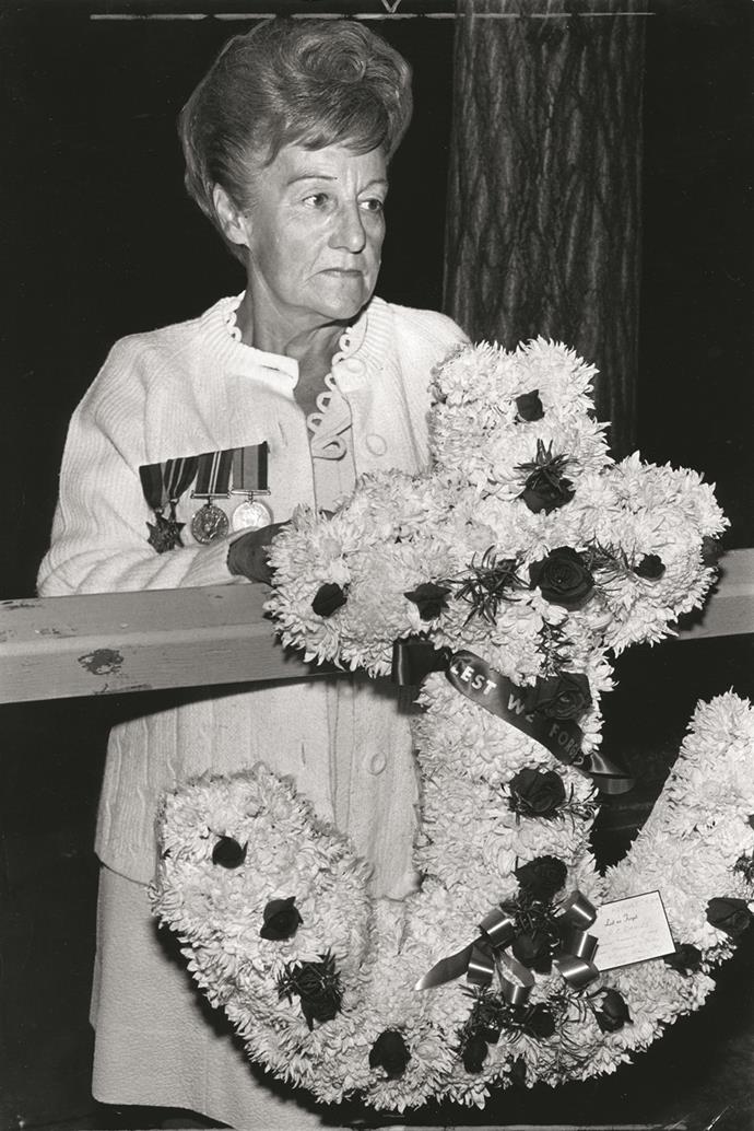 A woman wearing medals of honours hangs a wreath shaped as an anchor.
