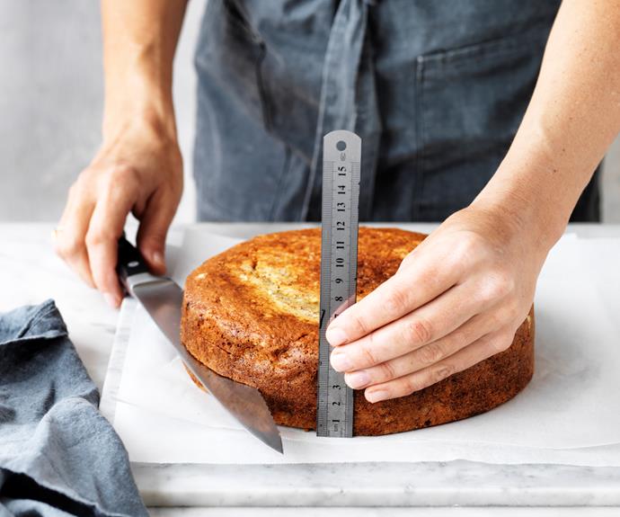 Holding a serrated knife horizontally, trim the top of cake to level. Using a ruler as a guide, make two small horizontal cuts, one-third and two-thirds of the way up the side of cake. Using the cut marks as a guide, cut to split cake into three equal layers