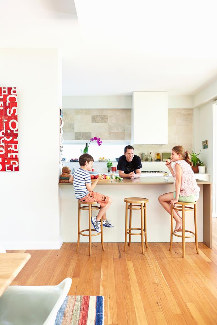 Patrick entertains Jim and Sophie in the kitchen. The family loves that that the area is partly enclosed with appliances and the pantry hidden behind the half wall. 

The **benchtop** is [Caesarstone](http://www.caesarstone.com.au/|target="_blank"). **Stools** from [Thonet](http://www.thonet.com.au/|target="_blank"). *Big Red* **artwork** by [Brett Coehlo](http://coelhoandco.com.au/|target="_blank").
