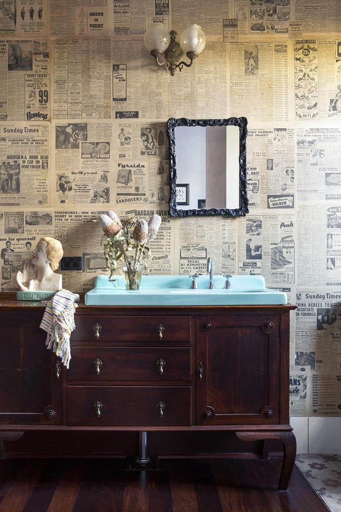 Newspapers found in the original home were upcycled into a one-off wallcovering. The vanity is made from an antique dresser, stained to match the kitchen cabinetry. The aqua enamel basin, sourced at a salvage yard, was one of the first items the couple found for the building project.