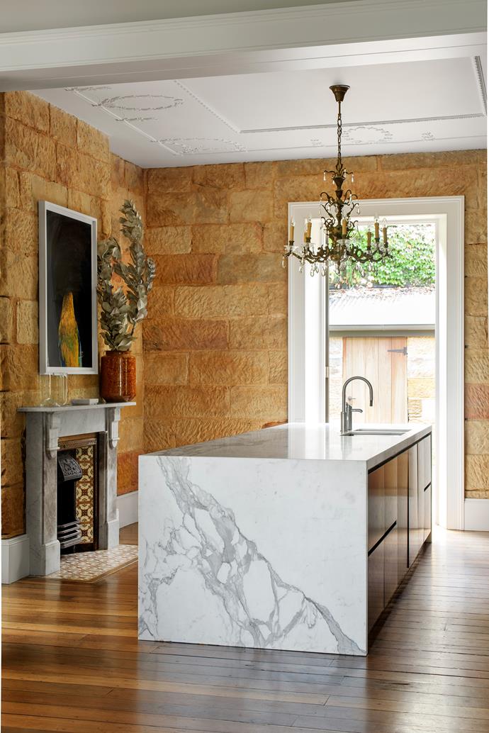 The kitchen is spare and monochrome to contrast with the warmth and texture of the abundant sandstone, with ebony-stained timber veneer and white marble. An antique chandelier hangs above the island.