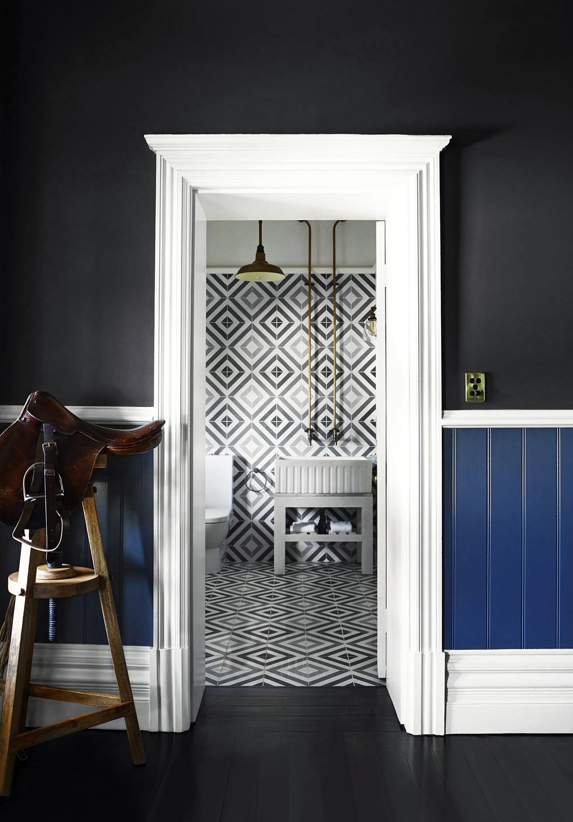 A dramatic powder-room is framed by a doorway in the hallway of a [horse stud homestead](https://www.homestolove.com.au/horse-stud-homestead-country-elegance-2416|target="_blank") redesigned by Greg Natale. A leather saddle on a timber stool is a reminder of the home's country setting.