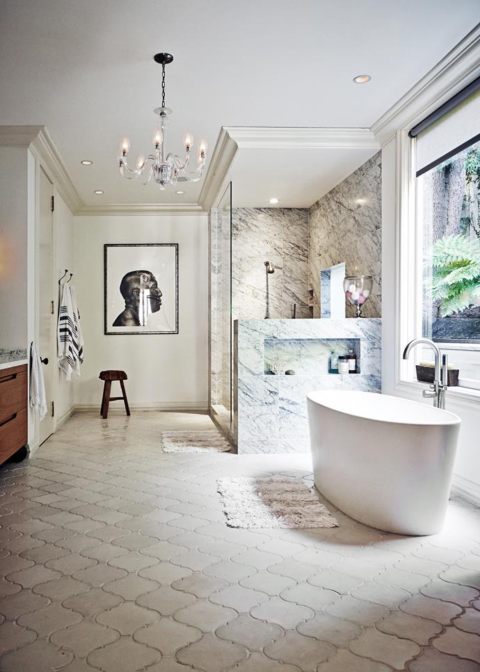 A glam antique chandelier and luxurious streamlined bath are juxtaposed with custom-made Moroccan floor tiles and rustic timber stool for an exotic touch.