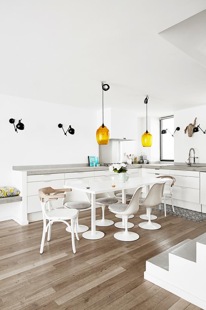While cupboards are from Ikea in the open-plan kitchen, concrete was poured for the benchtop. Jielde wall lamps continue from the living area around the kitchen. The custom-made table’s feet match the Tulip chairs.