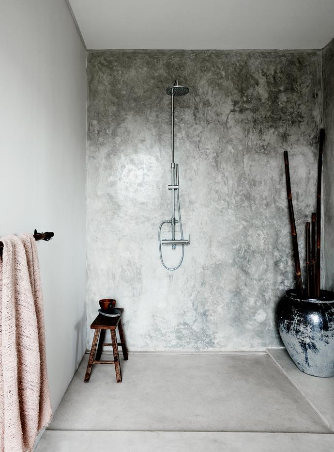 A Balinese-style cement bathroom is softened with bamboo towel rails and ornamental displays.