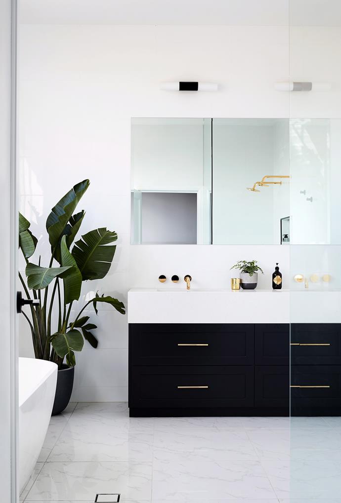[Indoor plants](https://www.homestolove.com.au/the-best-indoor-plants-to-suit-your-style-6625|target="_blank") help create a resort-like feel in a bathroom which will ensure you'll feel relaxed as soon as you enter. Here, large and small plants add life to this black and white bathroom, and help to highlight the striking golden finishes.
