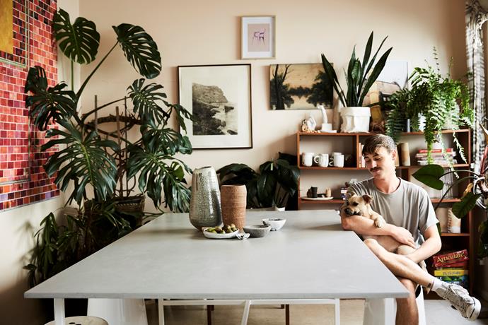 James and pooch Beatrix relax in the dining room of their share house, which is a beguiling jungle of plants and earthy ceramics.
