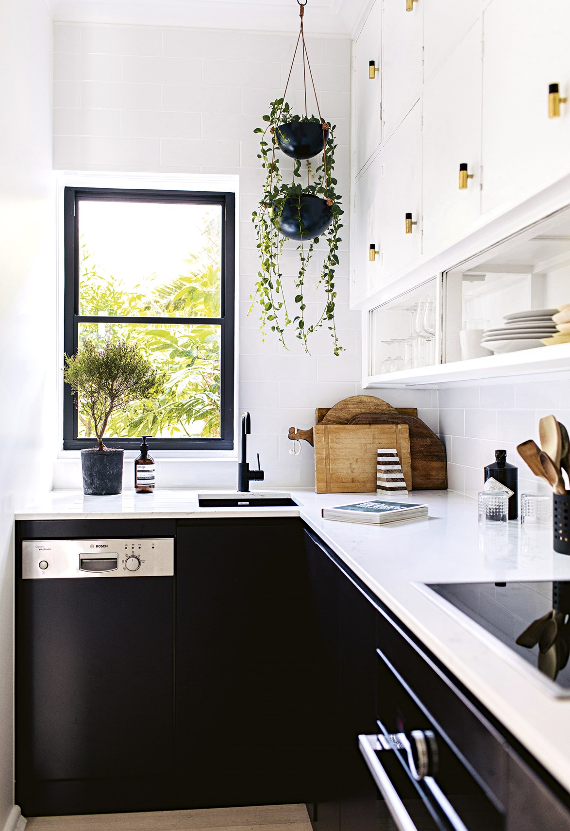In this small kitchen, black cabinetry has only been used below the benchtop to avoid the space feeling too closed in. A hanging plant helps to draw your eye up and create a sense of height and space.