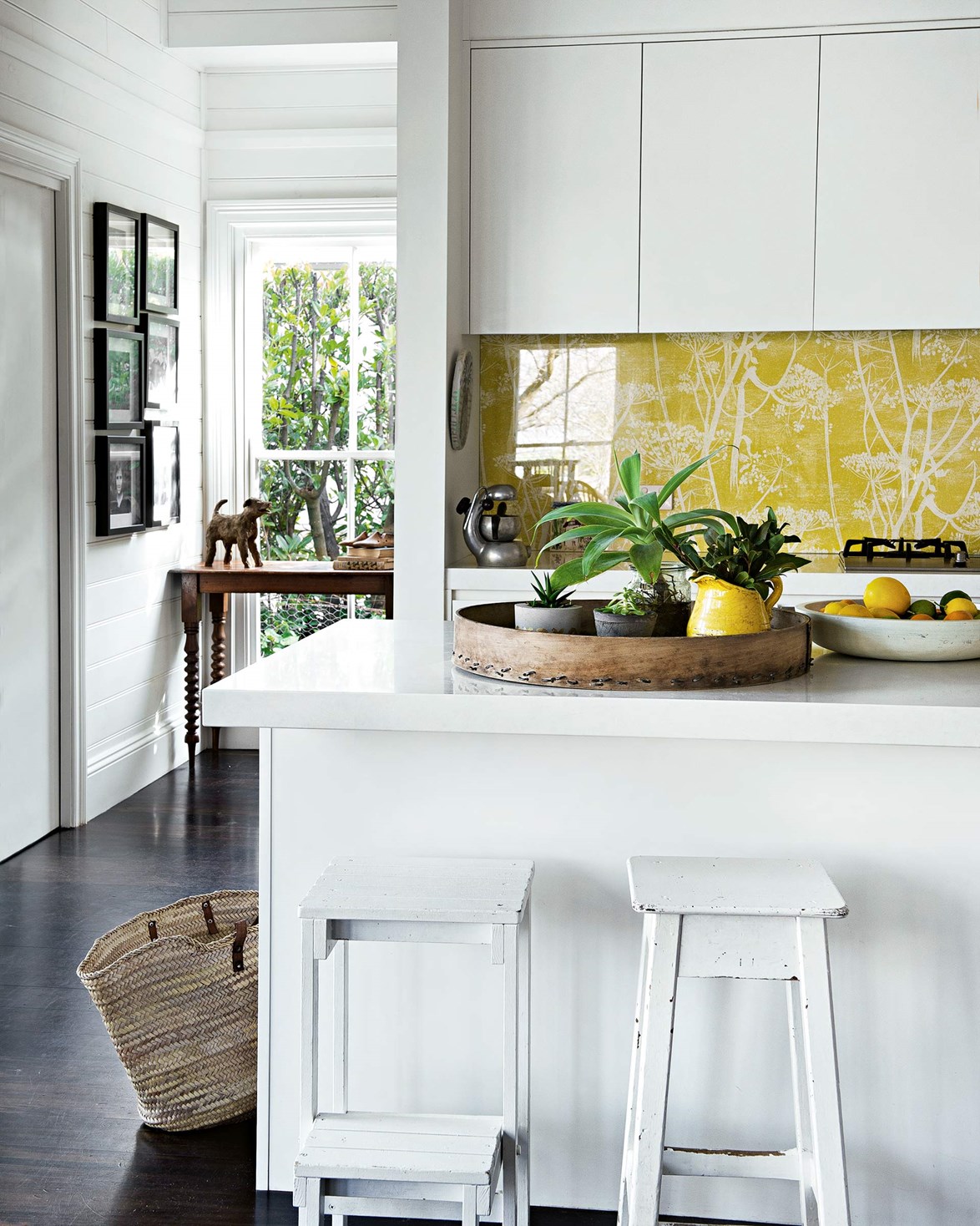 Starting at the front door, sunny pops of yellow are a recurring theme throughout this revamped [weatherboard cottage in Bowral](https://www.homestolove.com.au/weatherboard-cottage-in-bowral-13647|target="_blank"). In the kitchen, the owners opted for a glass splashback featuring Cole & Son wallpaper in Cow Pasture to bring colour, pattern and character into what could've been a sterile white room.
