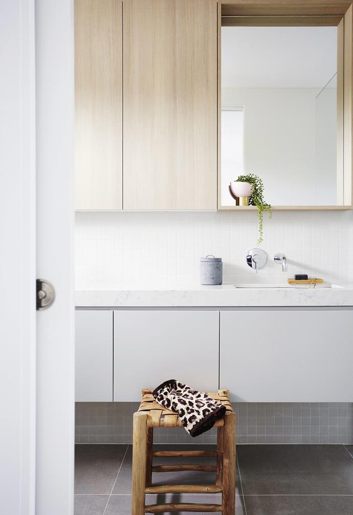 To ensure warm tones through [this white bathroom](https://www.homestolove.com.au/coastal-holiday-home-19311|target="_blank"), owners Joe and Olivia added blonde timber cabinetry and sweet styling accents via the leather and timber stool and cute leopard print hand towel.