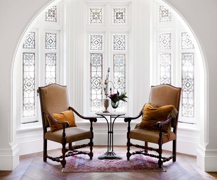Two antique armchairs in front of a lead light bay window
