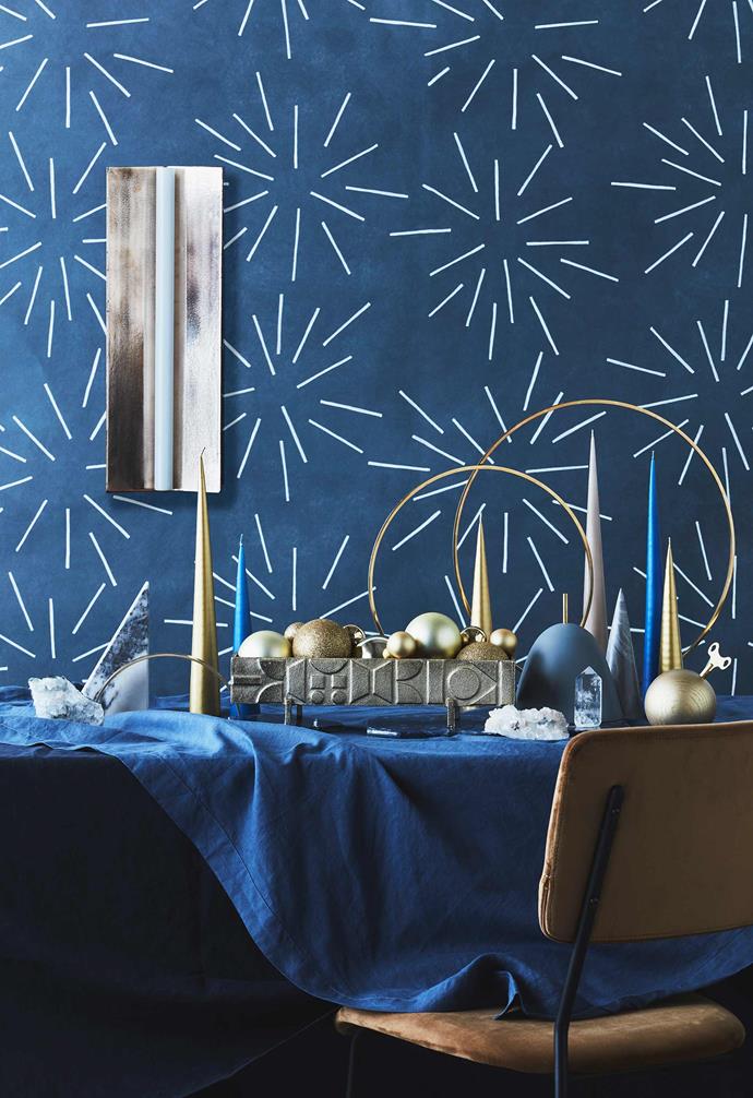 **Set to sparkle** Create a festive tablescape with ornaments and candles in a mix of shapes and heights. For the elegant modern scape, Jono paired deep navy tones with bright golds and minimalist tree shapes with some sparkle to add some sophistication to your table.<br>*Styling: Jono Fleming with assistance by Nonci Nyoni and Olivia Hutchinson | Photography: Maree Homer*.<br><br>**Get the look** 'Longton' wall light, $2695, [Volker Haug Studio](https://www.volkerhaug.com/|target="_blank"|rel="nofollow"). Linen tablecloths in French Blue, $110, and Navy, $205, [In Bed](https://inbedstore.com/|target="_blank"|rel="nofollow"). 'Apophyllite Cluster' crystal, $99, and Kristina Dam Studio 'Desk Sculptures' marble triangle and brass arch (part of a set of sculptures), $269/set of 4,  [The Minimalist](https://www.theminimalist.com.au/|target="_blank"|rel="nofollow"). Ester + Erik 'Cone' candles in Gold, $21, Blue, $14.50, and Nougat, $15.50, [Top3 By Design](http://top3.com.au/|target="_blank"|rel="nofollow"). 'Pictograph' centrepiece, $79, [West Elm](http://www.westelm.com.au/|target="_blank"|rel="nofollow"). Gold baubles (In centrepiece), [Big W](https://www.bigw.com.au/|target="_blank"|rel="nofollow"). Stoned 'Sodalite' quartz trivet, $149, and 'Sodalite' quartz tray, $379, [Top3 By Design](http://top3.com.au/|target="_blank"|rel="nofollow"). 'Gloria' brass ring candleholders, $275/small and $350/large, [Great Dane](https://greatdanefurniture.com/|target="_blank"|rel="nofollow"). 'Pink Apophyllite Cluster' crystal, $119,  [The Minimalist](https://www.theminimalist.com.au/|target="_blank"|rel="nofollow"). 'Gomma' storage box, $195, [Great Dane](https://greatdanefurniture.com/|target="_blank"|rel="nofollow"). 'Clear Quartz' crystal, $49,  [The Minimalist](https://www.theminimalist.com.au/|target="_blank"|rel="nofollow"). Zakkia 'Concrete' cone, $29, [Clickon Furniture](https://www.clickonfurniture.com.au/|target="_blank"|rel="nofollow"). Siebensachen 'Mozart Kugel' musical orb, $159, [Designstuff](https://www.designstuff.com.au/|target="_blank"|rel="nofollow"). 'Hooper' dining chair, $405, [Globe West](https://www.globewest.com.au/|target="_blank"|rel="nofollow"). 'Festival' wallpaper in Oyster, $72/lineal metre, [These Walls](https://thesewalls.com.au/|target="_blank"|rel="nofollow").